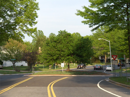 photo shows an intersection on a residential street 4 lanes wide, including 2 parking lanes.  The corners are very rounded.  In the middle of the intersection is a circle that is wider than the street, so it extends into the side street, leaving only a narrow lane between the circle and the corners.